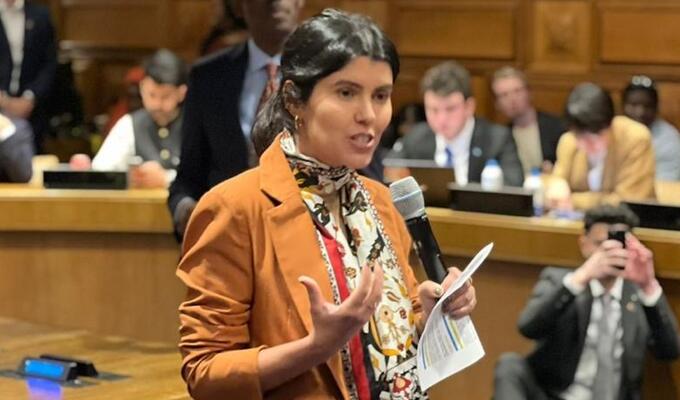 Woman in brown jacket stands to speak at UN forum