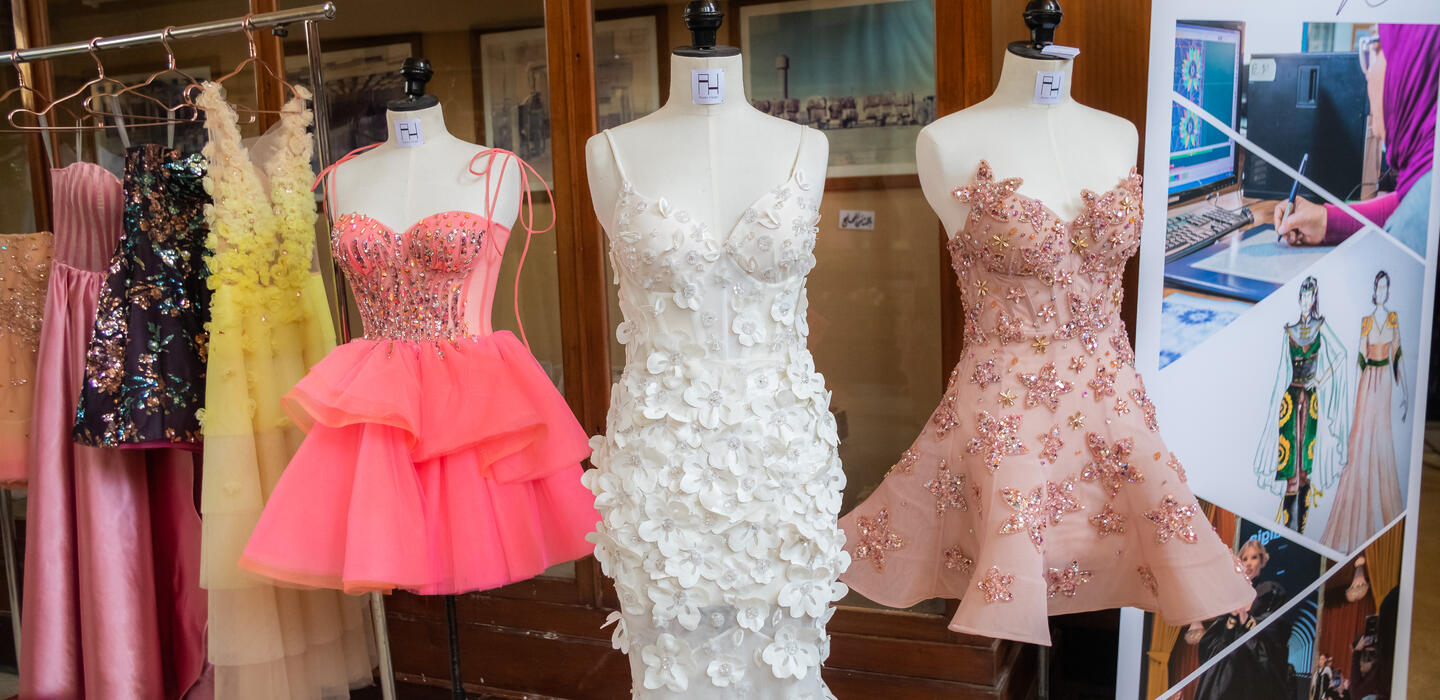 Three evening dresses displayed on mannequins (foreground) and 3 on hanging racks (background).