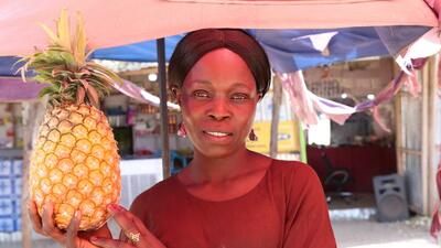 South Sudanese farmer holds pineapple at market stall in Juba