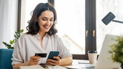 Woman entrepreneur smiles, sitting at laptop and holding credit card