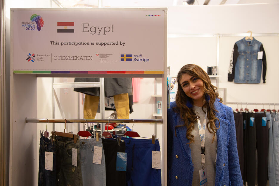 Une femme égyptienne se tient à côté d'un présentoir de vêtements lors d'une foire commerciale.