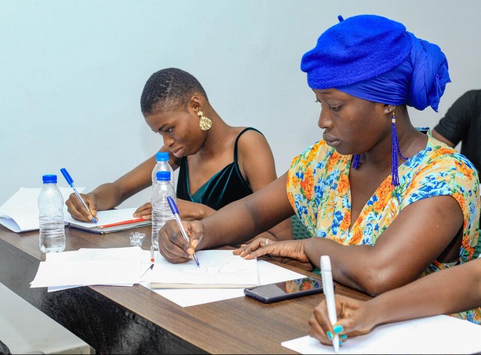 Two women, one weaing a blue headwrap, sit at desk in training session