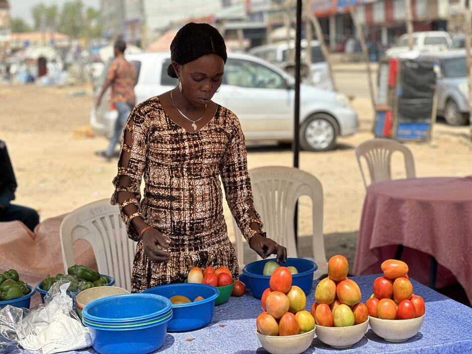 South Sudanese woman organises tomatoes in a market stall.