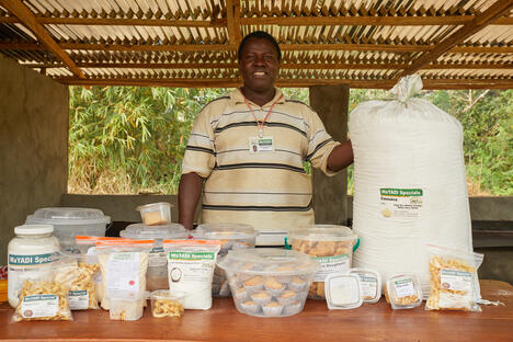 Man in market stall in Sierra Leone displays pastries in plastic bins