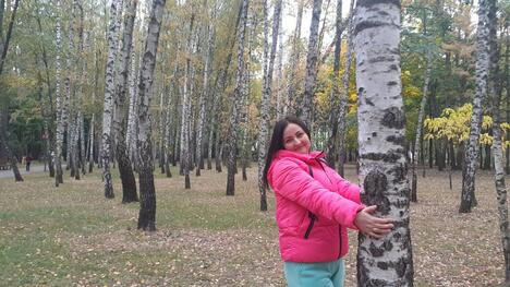 Woman in pink puffer jacket hugs a tree trunk