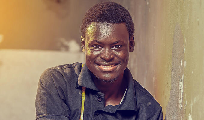 Homme africain souriant, assis et tourné vers l'avant, les bras à droite de l'image, installant une prise électrique.