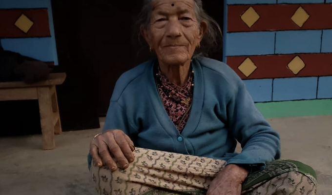 Elderly Nepalese woman sits on stoop on her her farm