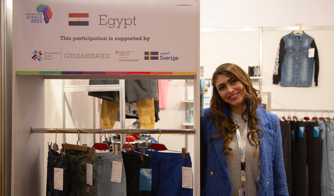 Egyptian businesswoman stands next to ITC display for textile business at trade show