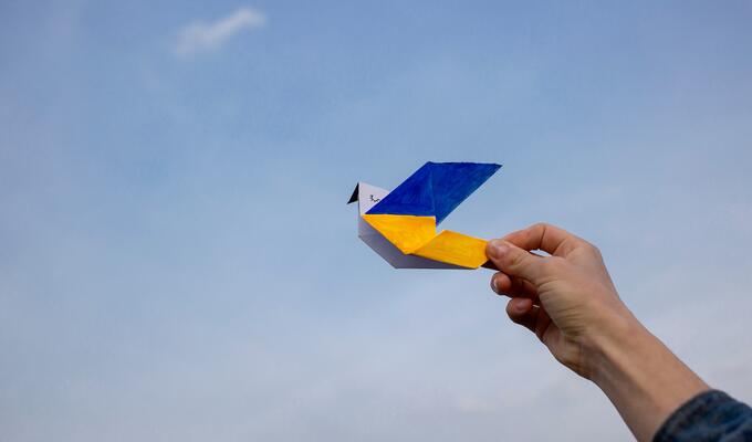 Origami bird in colours of Ukrainian flag held against sky