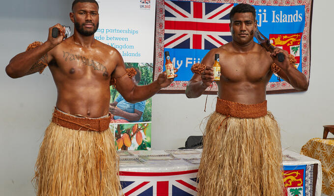Two men from Fiji wear traditional dress to display hot sauce bottles