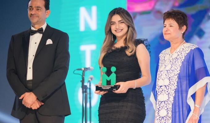Jordanian woman in format wear stands on stage to accept award from two other people