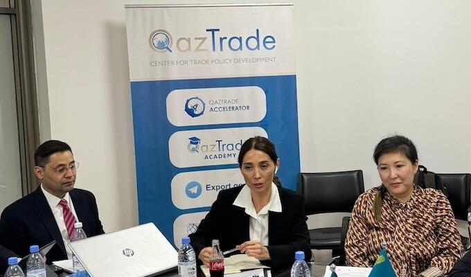 Three trade officials sit at table in front of banner reading QazTrade