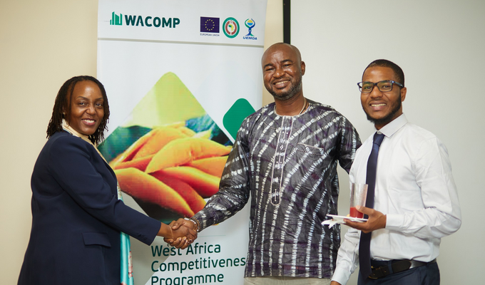 Three people shake hands in front of banner reading "West Africa Competitiveness Programme"