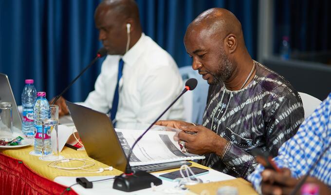 Man in West African print shirt sits behind microphone at conference table