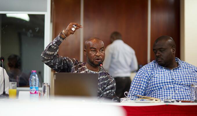Man in West African print shirt raises hand as he speaks in conference room