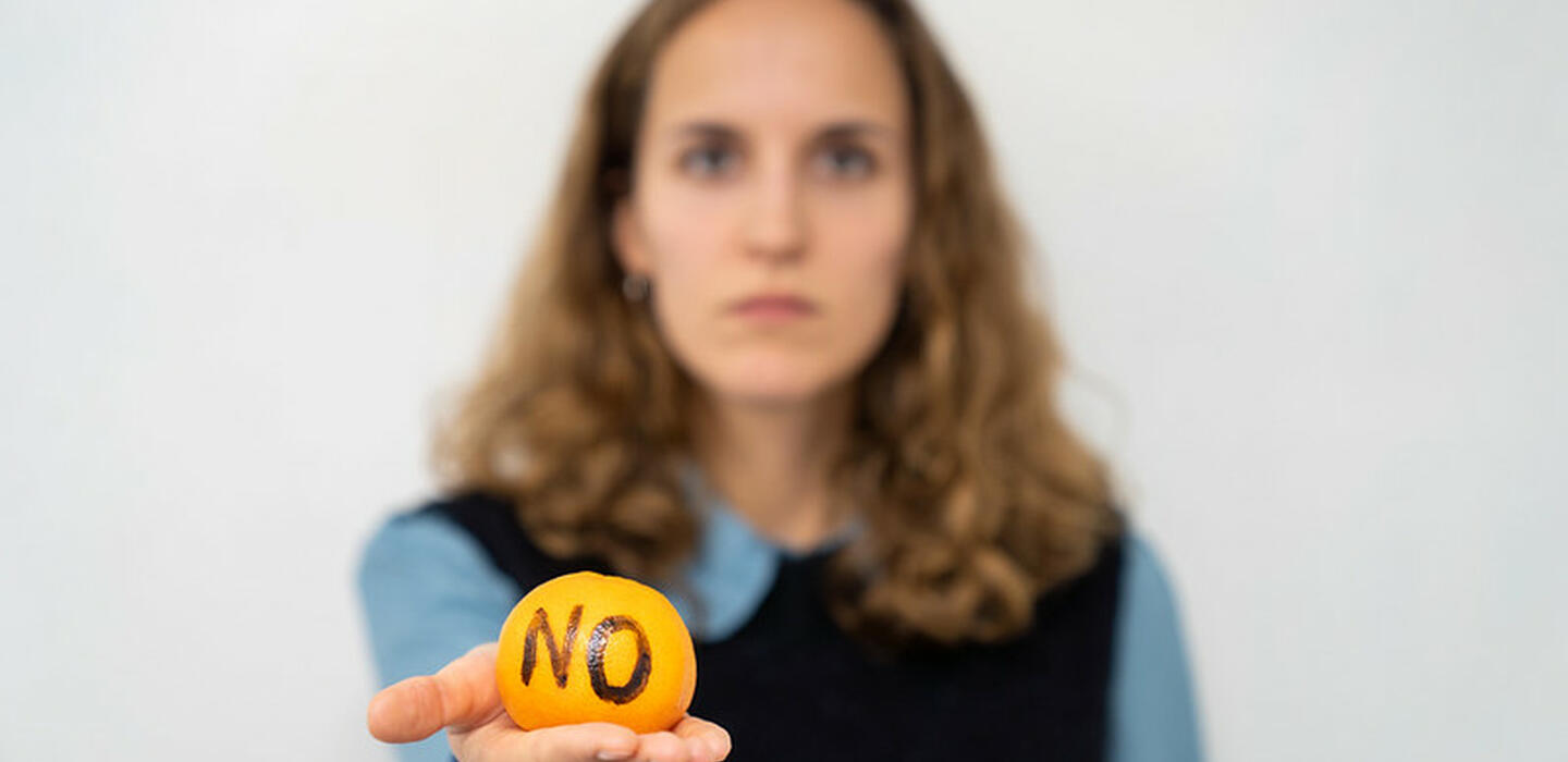 Blurred woman in background holding a clementine with NO written on it in foreground, in focus