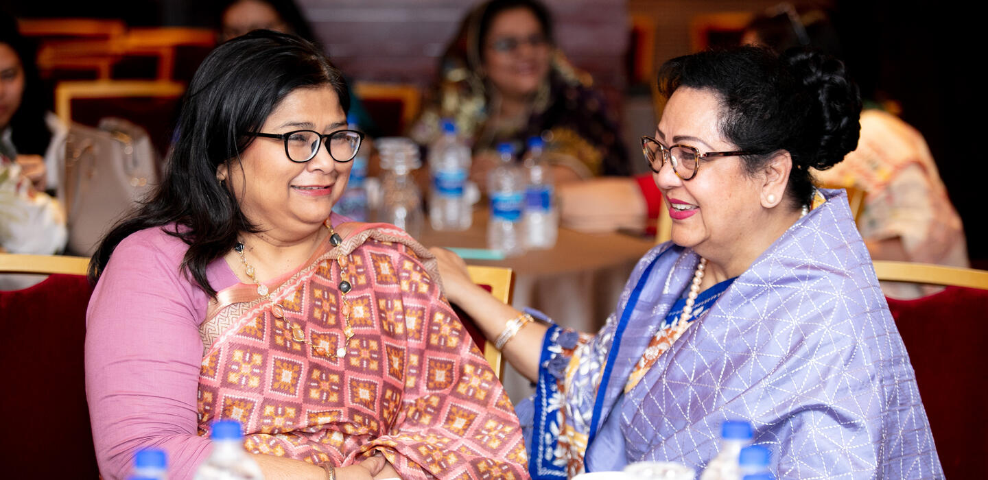Two Bangladeshi women speak to each other at table in conference room