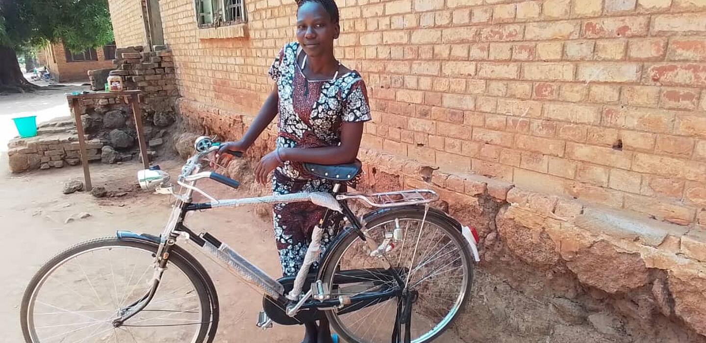 A South Sudanese farmer is standing with her bicycle