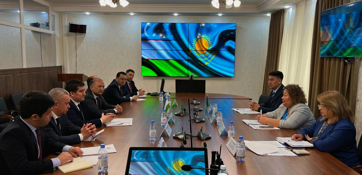 Uzbek and Kazakh trade officials sit at table with large screen on wall