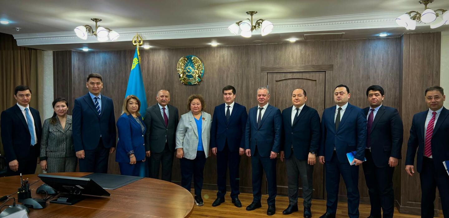 Uzbek and Kazakh trade officials in business attire, stand in front of dark wall with symbols of each country