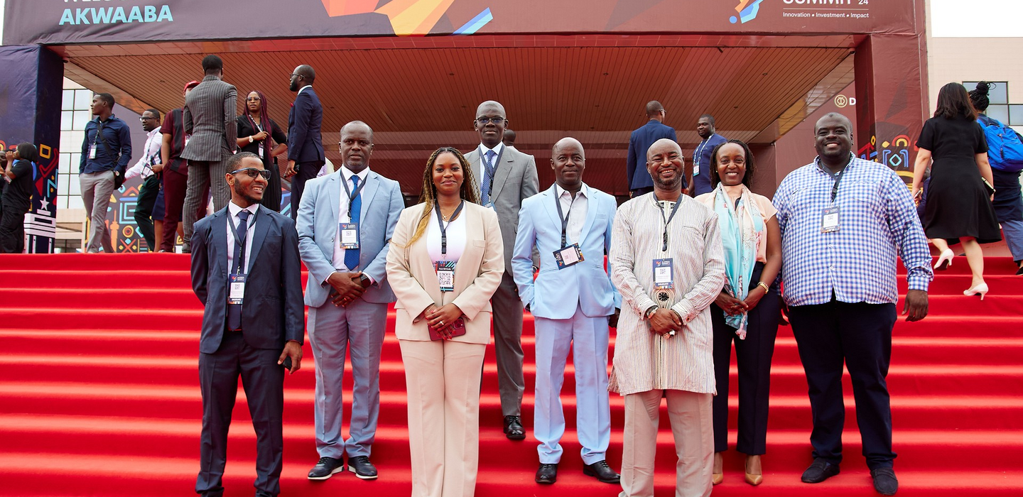 Eight West African business people pose in front of a white banner, reading in part “3i Africa Summit” 