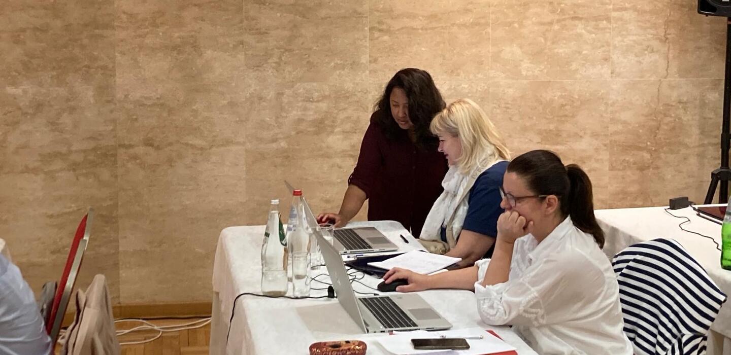 Woman leans over a laptop to assist a workshop participant
