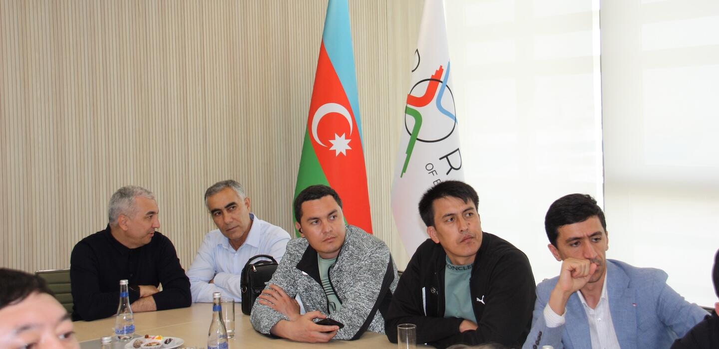 Five men sit at table with flag of Azerbaijan in background