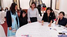 Group of women huddle around table reviewing data gathered by SheTrades