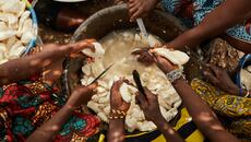 West African women slice cassava over a bucket